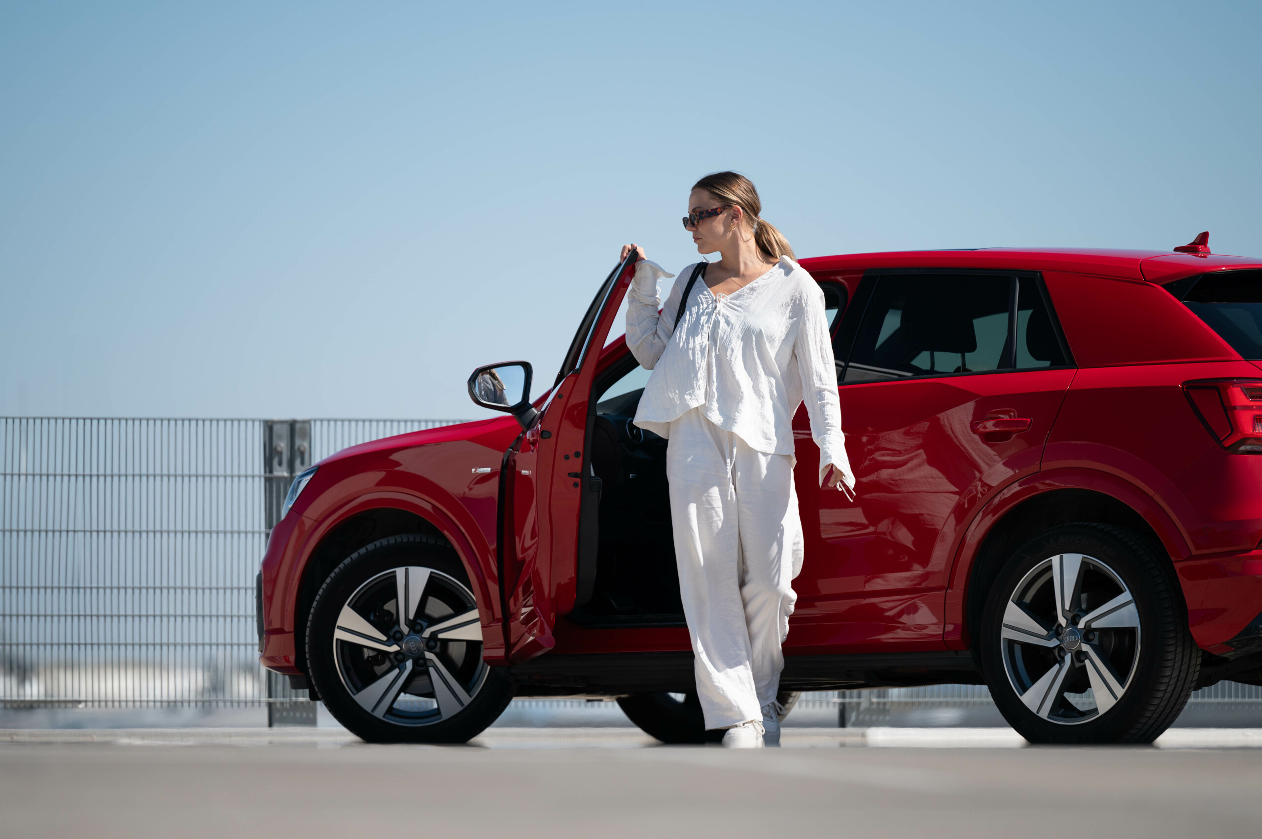 Frau mit Sonnenbrille vor einem roten Audi Q2